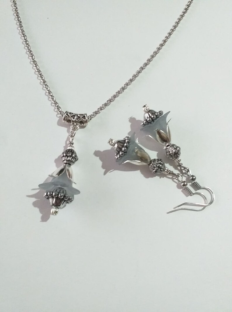 May include: A silver necklace and earrings set with a delicate flower design. The necklace features a silver chain with a flower pendant, while the earrings have a flower dangle with a silver hook.