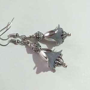 May include: A pair of silver earrings with grey flower-shaped charms. The charms have a silver bead detail and are attached to a silver hook.