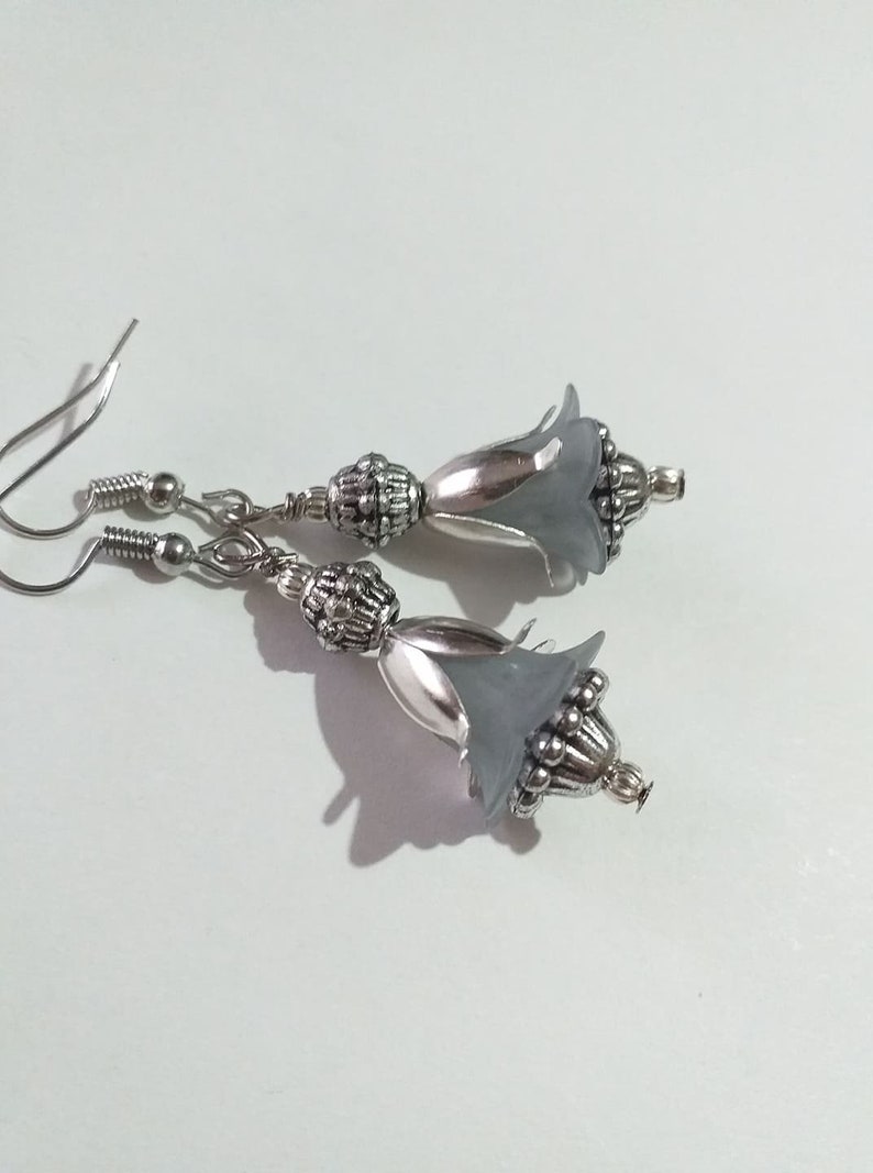 May include: A pair of silver earrings with grey flower-shaped charms. The charms have a silver bead detail and are attached to a silver hook.