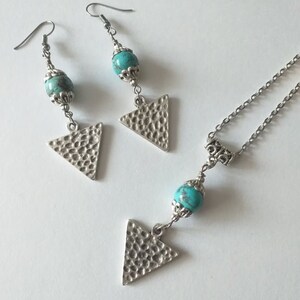 May include: A turquoise and silver necklace and earrings set with triangle pendants. The necklace has a silver chain and a turquoise bead. The earrings have silver hooks and turquoise beads.