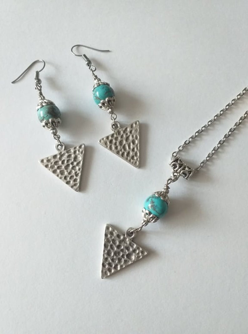 May include: A turquoise and silver necklace and earrings set with triangle pendants. The necklace has a silver chain and a turquoise bead. The earrings have silver hooks and turquoise beads.