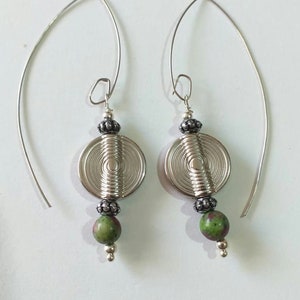 Può includere: Orecchini d'argento con una pietra verde e un design circolare. Gli orecchini sono realizzati in filo e hanno un design semplice ed elegante.