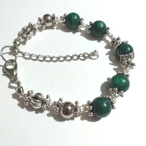 May include: A silver bracelet with green malachite beads and silver accents. The bracelet has a lobster clasp closure.