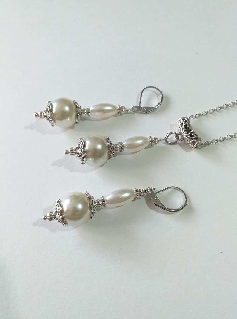 May include: A set of pearl earrings and a necklace with silver accents. The earrings have a large pearl bead and a smaller pearl bead, while the necklace has a single large pearl bead.