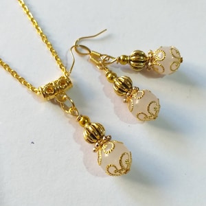 May include: A gold necklace and earrings set with white beads and gold filigree accents.