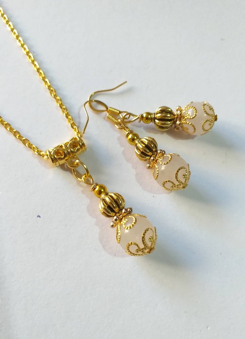 May include: A gold necklace and earrings set with white beads and gold filigree accents.