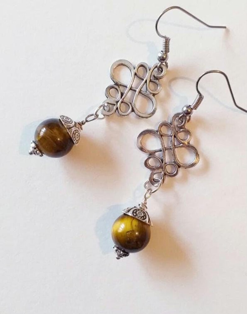May include: A pair of silver earrings with a knotted design and a round tiger's eye stone dangle.