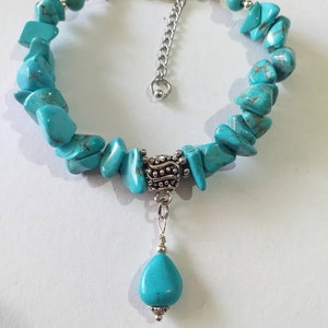 May include: Turquoise gemstone bracelet with a silver charm and a teardrop-shaped pendant. The bracelet is made of irregular shaped turquoise stones and has a silver clasp.