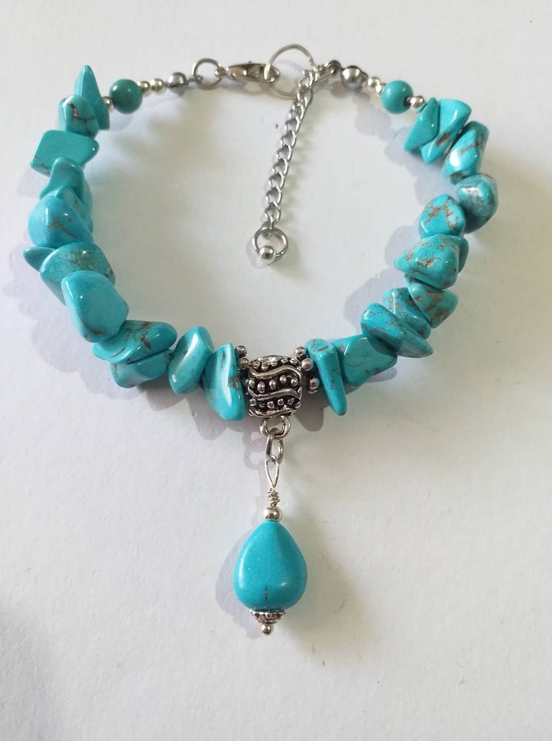 May include: Turquoise gemstone bracelet with a silver charm and a teardrop-shaped pendant. The bracelet is made of irregular shaped turquoise stones and has a silver clasp.