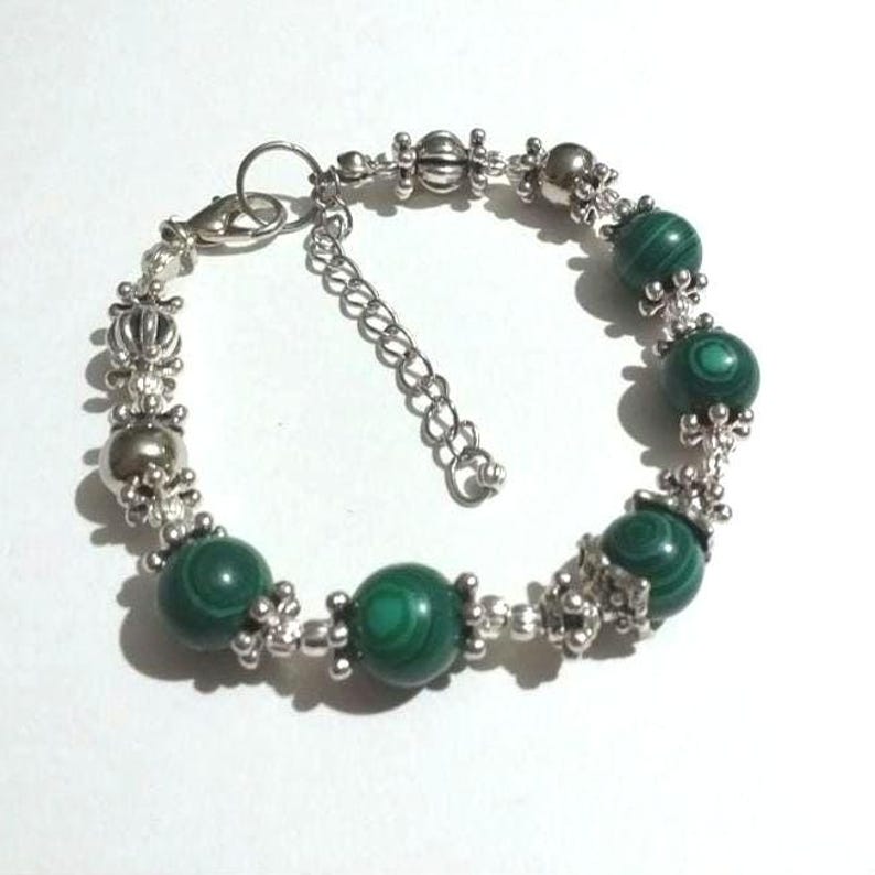 May include: A silver bracelet with green malachite beads and silver accents. The bracelet has a clasp closure.