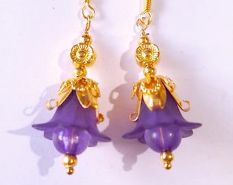 May include: Purple flower shaped dangle earrings with gold accents. The earrings have a hook fastening.