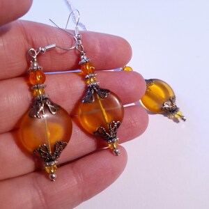 May include: A pair of amber glass drop earrings with silver filigree accents. The earrings are suspended from silver hooks.