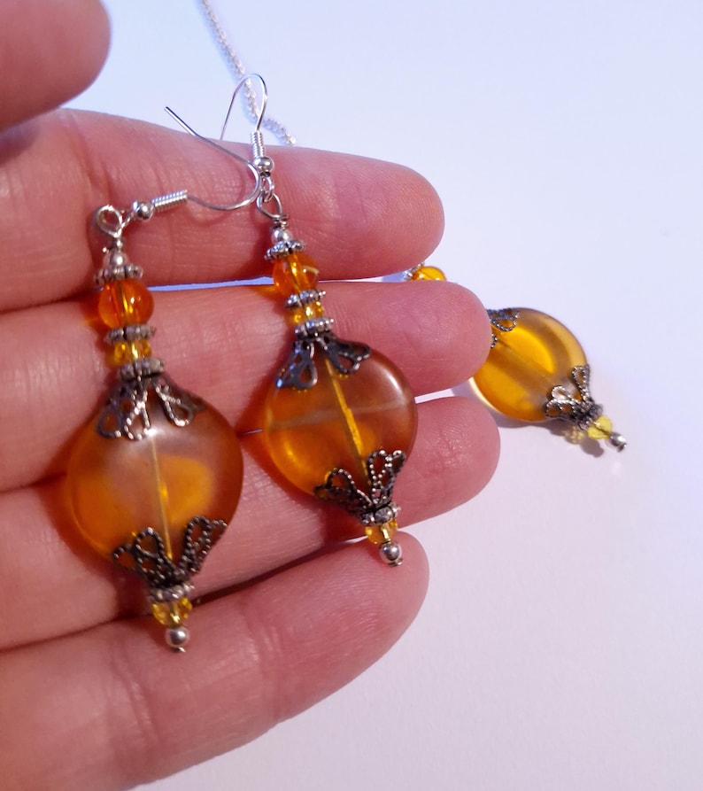 May include: A pair of amber glass drop earrings with silver filigree accents. The earrings are suspended from silver hooks.