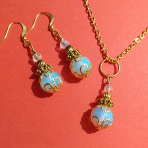 May include: A gold necklace and earrings set with a blue and white opal pendant and matching earrings. The pendant and earrings have a gold filigree design.