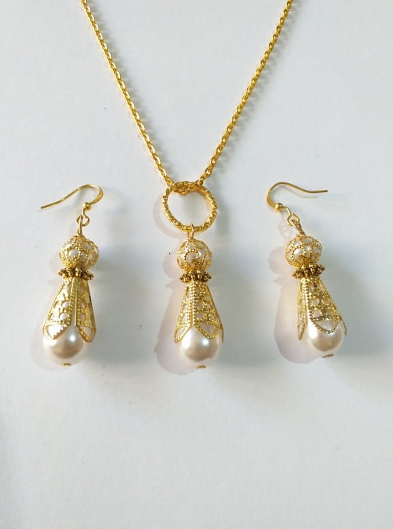 May include: A gold necklace with a circular pendant and matching earrings. The pendant and earrings feature a delicate filigree design and a white pearl drop.