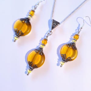 May include: A set of amber glass earrings and a necklace with silver chain and pendant. The earrings and pendant feature a filigree design and are accented with small clear beads.