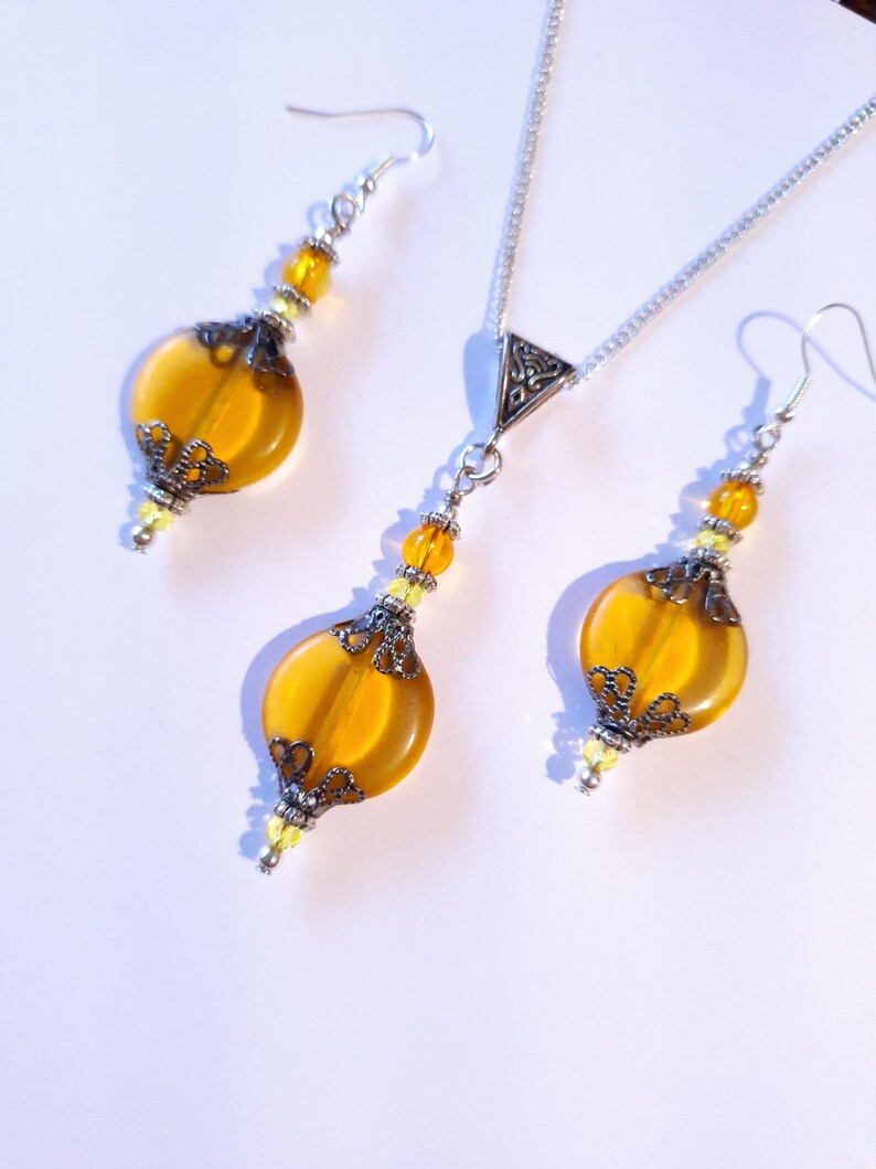 May include: A set of amber glass earrings and a necklace with silver chain and pendant. The earrings and pendant feature a filigree design and are accented with small clear beads.