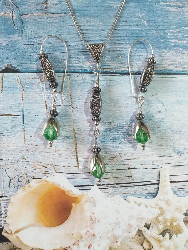 May include: A silver necklace and earrings set with green glass beads and silver filigree accents. The necklace has a pendant with a teardrop-shaped green glass bead.
