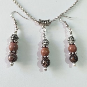 May include: A silver chain necklace with a silver pendant and three brown and black stone beads. Matching earrings with three brown and black stone beads.