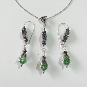 May include: A silver necklace with a pendant and matching earrings. The pendant and earrings feature a green glass teardrop shape with silver accents.