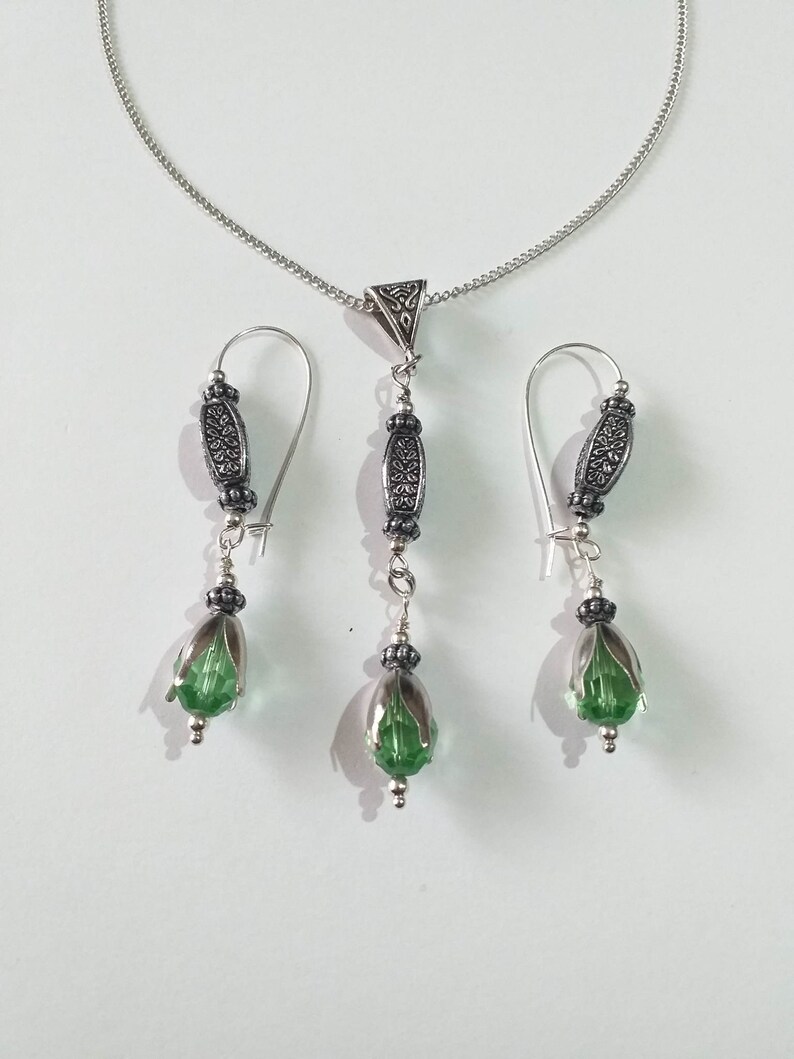 May include: A silver necklace with a pendant and matching earrings. The pendant and earrings feature a green glass teardrop shape with silver accents.