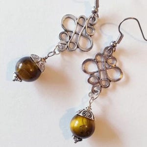 May include: A pair of silver earrings with a knotted design and a brown tiger's eye stone bead on each earring.