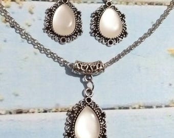 May include: A silver necklace and earrings set with a teardrop-shaped pendant and matching earrings. The pendant and earrings feature a white opal-like stone set in a filigree design.