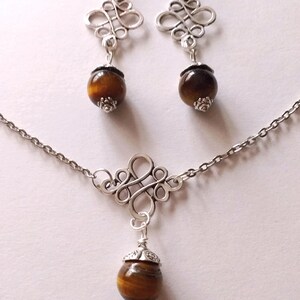 May include: A silver necklace and earrings set with a brown tiger's eye stone pendant and matching earrings. The pendant and earrings feature a decorative, intricate, silver design.