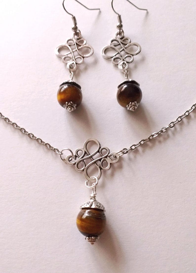 May include: A silver necklace and earrings set with a brown tiger's eye stone pendant and matching earrings. The pendant and earrings feature a decorative, intricate, silver design.