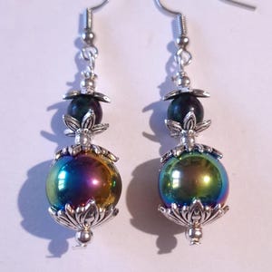 Op de afbeelding: Een paar zilveren oorbellen met regenboogkleurige, iriserende ronde kralen en zwarte kralen met zilveren bloemmotieven.