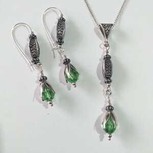 May include: A silver necklace and earrings set with green crystal teardrop beads and silver filigree accents.