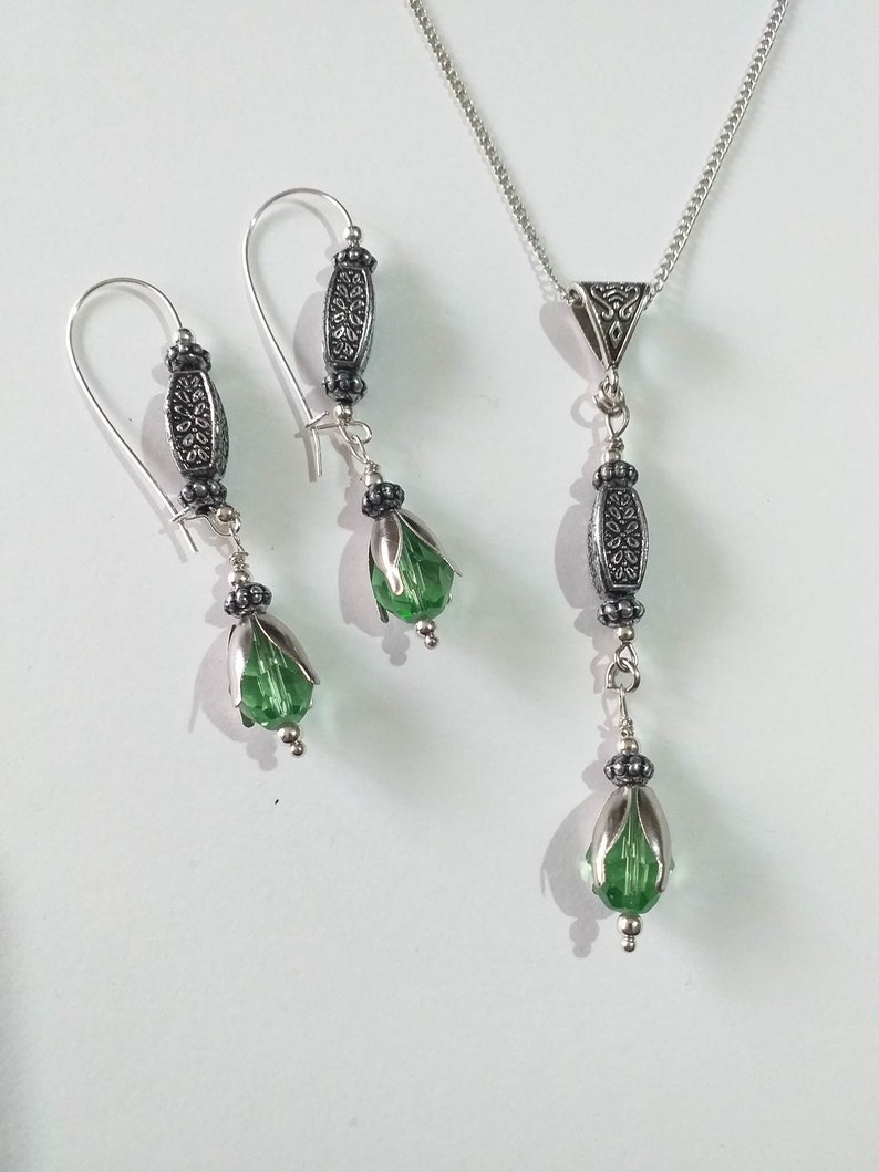 May include: A silver necklace and earrings set with green crystal teardrop beads and silver filigree accents.