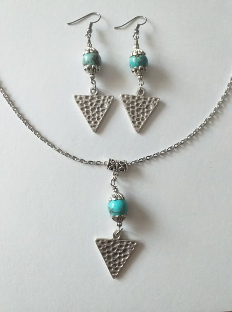 May include: A silver necklace and earrings set with turquoise beads and triangle pendants. The triangle pendants have a hammered texture.