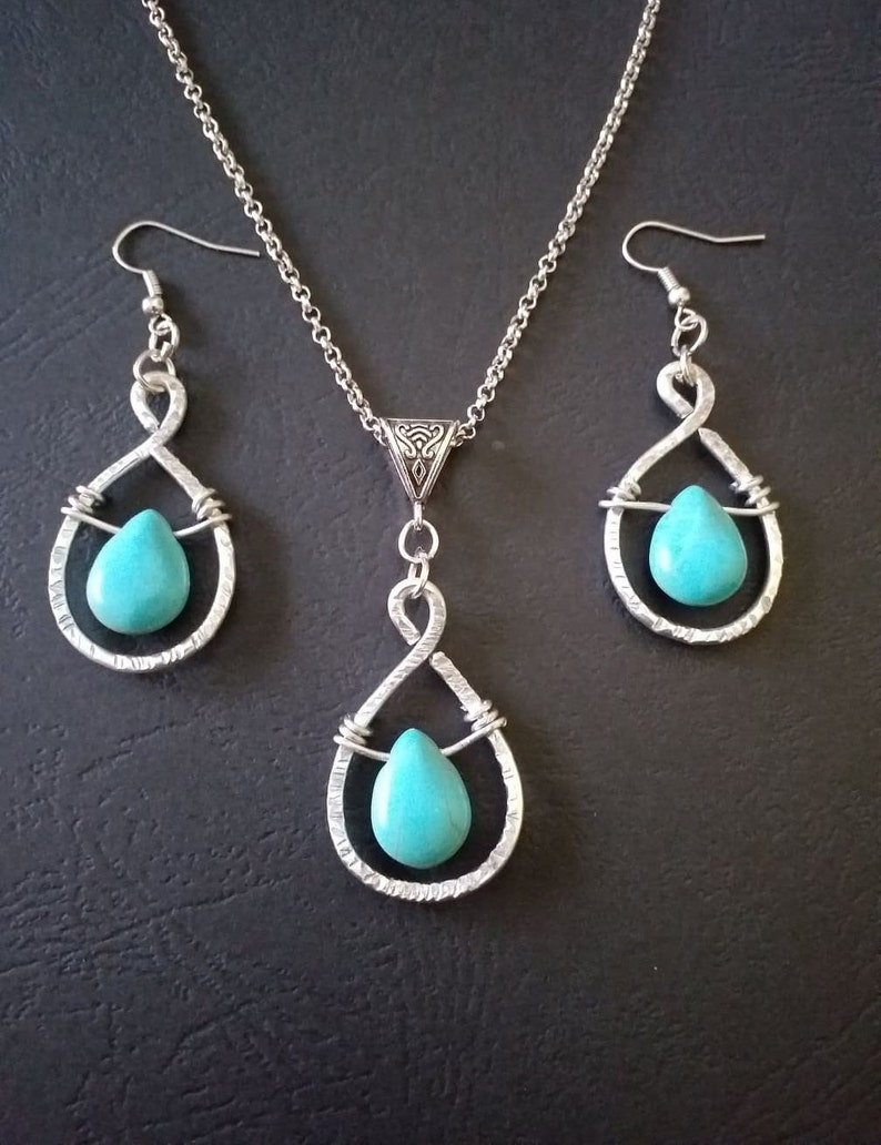 K&ouml;nnte beinhalten: Ein silbernes Halsketten- und Ohrring-Set mit t&uuml;rkisfarbenen Tr&auml;nensteinen. Halskette und Ohrringe haben ein zartes, gedrehtes Drahtdesign.