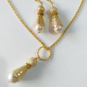 May include: A gold necklace and earrings set with a pearl drop pendant and matching earrings. The necklace has a delicate chain and a small circle charm. The earrings have a filigree design.