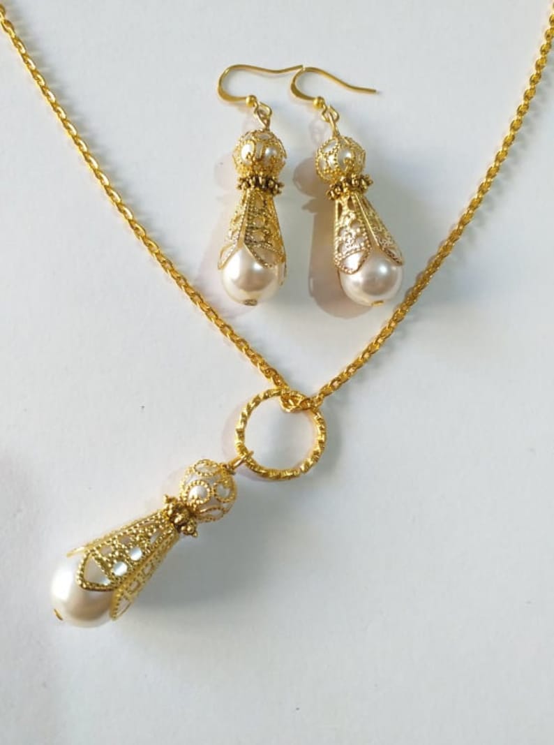 May include: A gold necklace and earrings set with a pearl drop pendant and matching earrings. The necklace has a delicate chain and a small circle charm. The earrings have a filigree design.