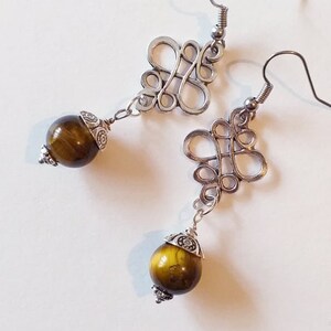 May include: Silver earrings with a decorative knot design and a round, brown tiger's eye stone dangle.