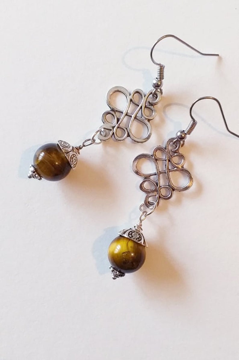 May include: Silver earrings with a decorative knot design and a round, brown tiger's eye stone dangle.