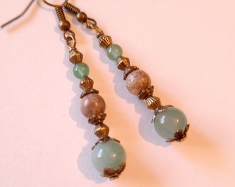May include: A pair of long, dangle earrings with green and brown beads. The earrings have a brass finish and feature a variety of bead shapes and sizes.