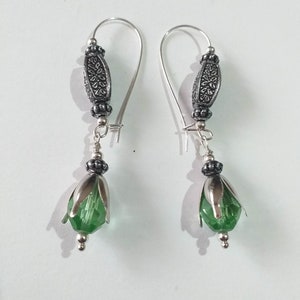 May include: A pair of silver earrings with green glass flower-shaped beads and silver filigree accents.