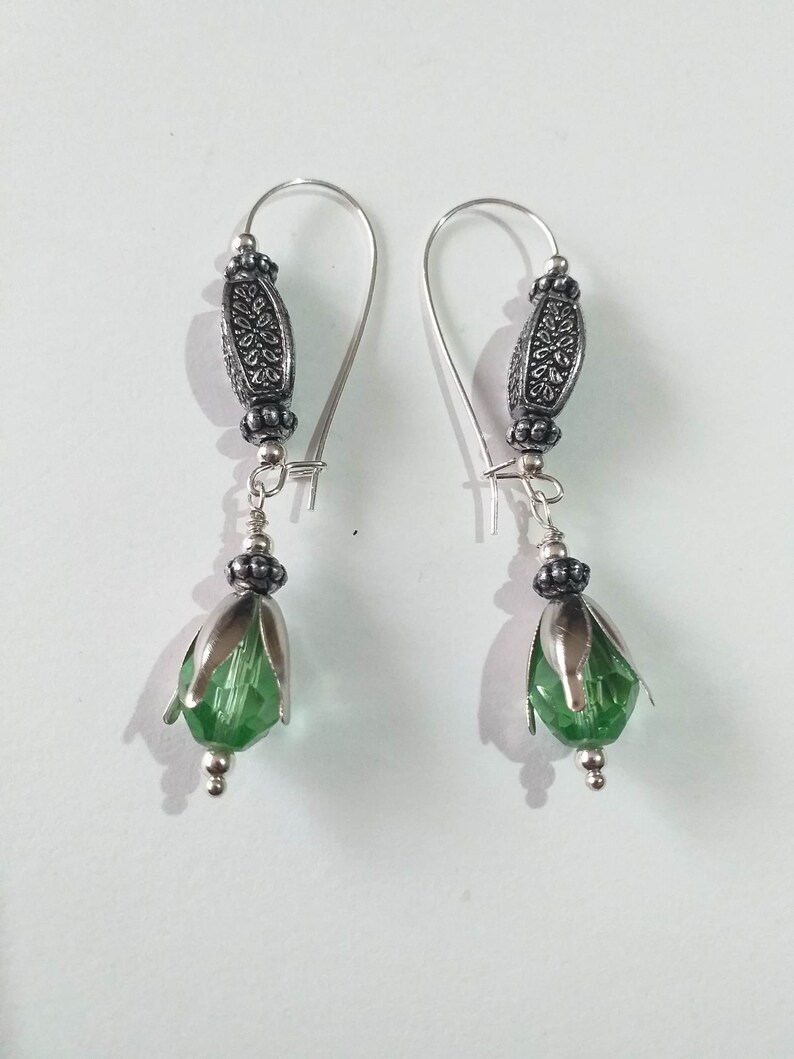 May include: A pair of silver earrings with green glass flower-shaped beads and silver filigree accents.