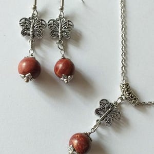 May include: A silver necklace and earrings set with red stone beads and butterfly charms.