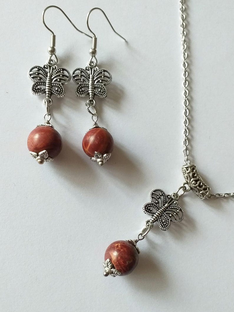 May include: A silver necklace and earrings set with red stone beads and butterfly charms.