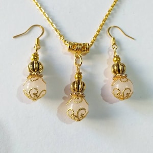 May include: A gold necklace and earrings set with a delicate chain and white stone pendants. The pendants feature a gold filigree design.