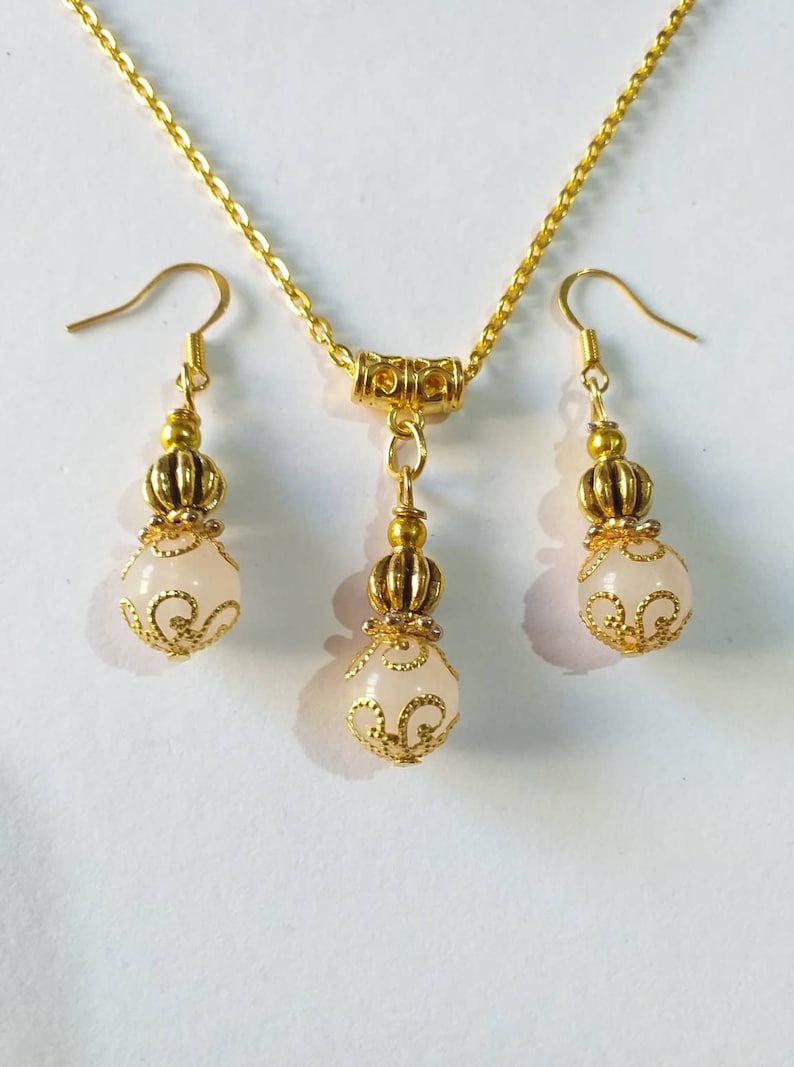 May include: A gold necklace and earrings set with a delicate chain and white stone pendants. The pendants feature a gold filigree design.
