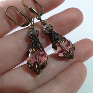 Op de afbeelding: Een paar oorhangers met roze gefacetteerde glazen kralen en antieke bronzen filigraan accenten.