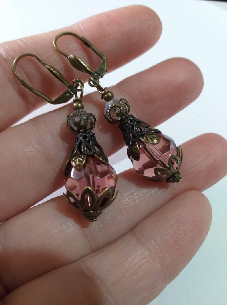 Op de afbeelding: Een paar oorhangers met roze gefacetteerde glazen kralen en antieke bronzen filigraan accenten.