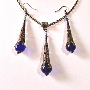 May include: A set of blue glass and bronze earrings and necklace. The earrings and necklace feature a teardrop-shaped blue glass bead with a bronze filigree design.