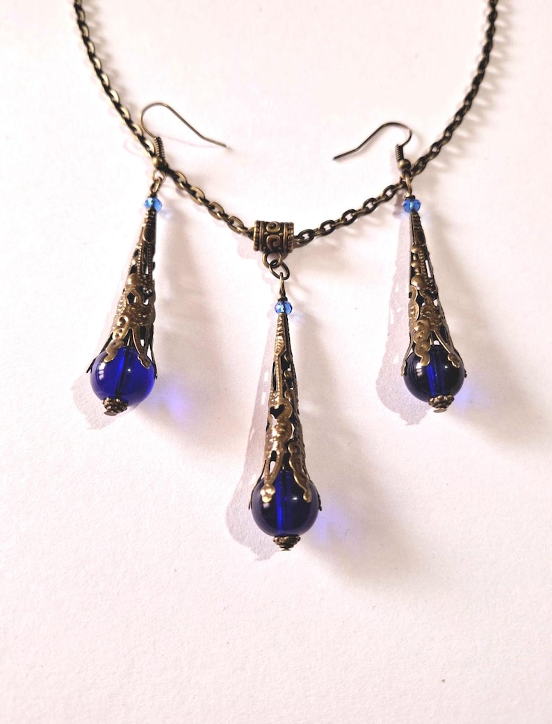 May include: A set of blue glass and bronze earrings and necklace. The earrings and necklace feature a teardrop-shaped blue glass bead with a bronze filigree design.