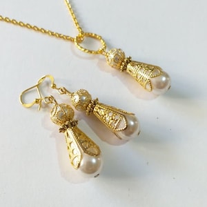 May include: A gold necklace and earrings set with a delicate chain and pearlescent teardrop pendants. The pendants feature intricate filigree designs.